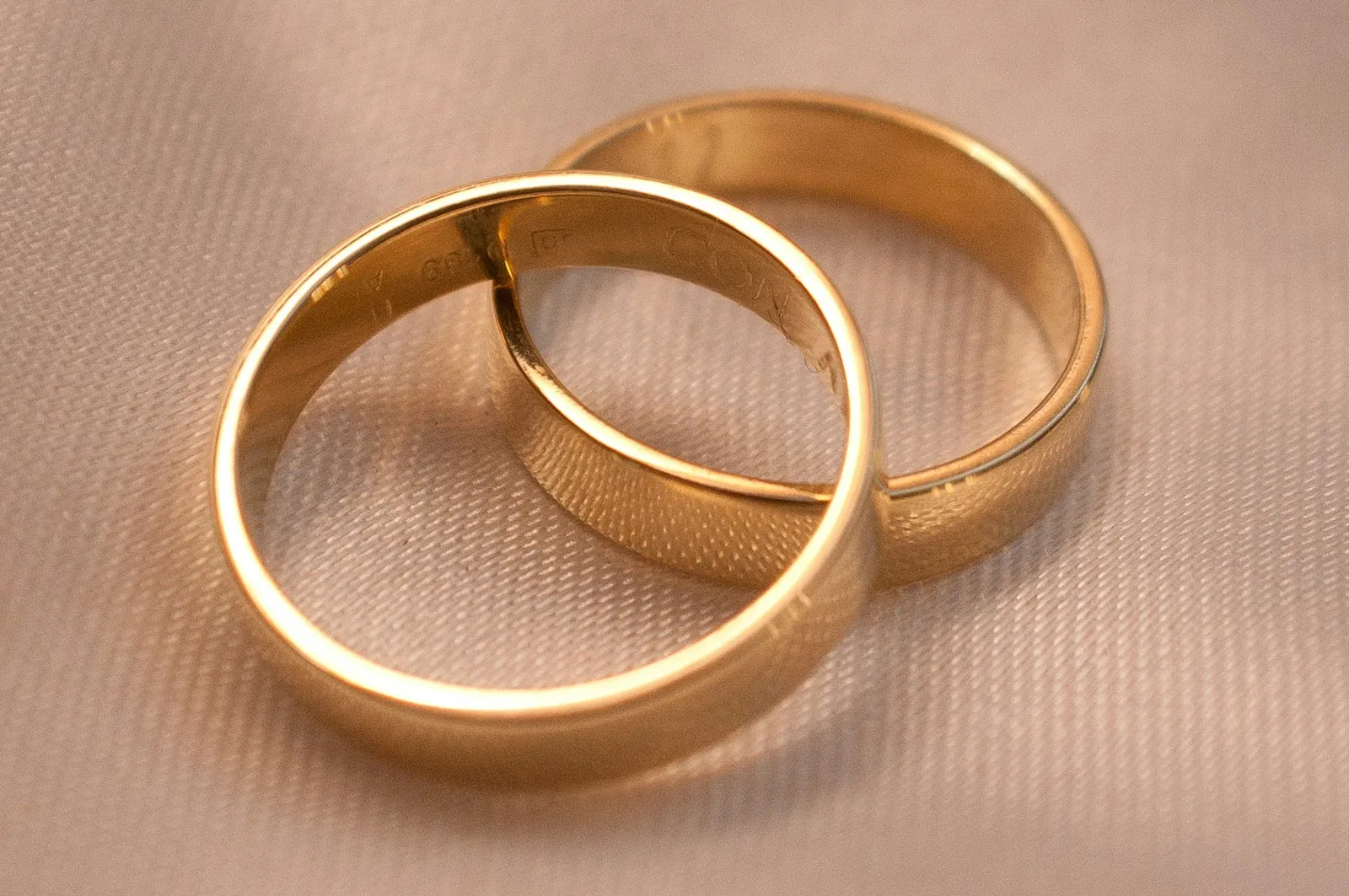 Dua cincin kawin emas kuning saling bertaut di atas kain krem